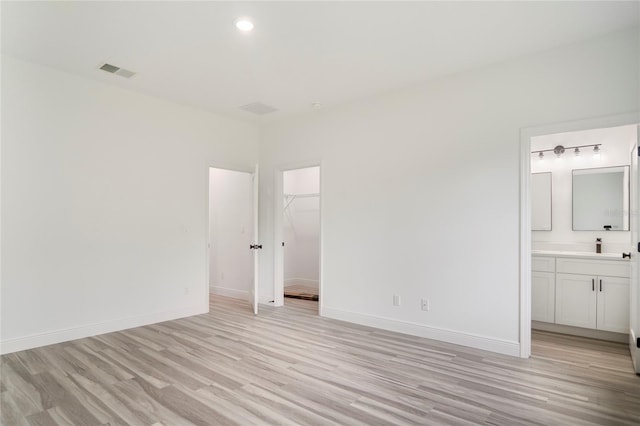 unfurnished bedroom featuring connected bathroom, a closet, light hardwood / wood-style flooring, and a spacious closet