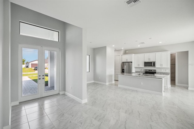 kitchen featuring light stone countertops, appliances with stainless steel finishes, sink, a center island with sink, and white cabinets