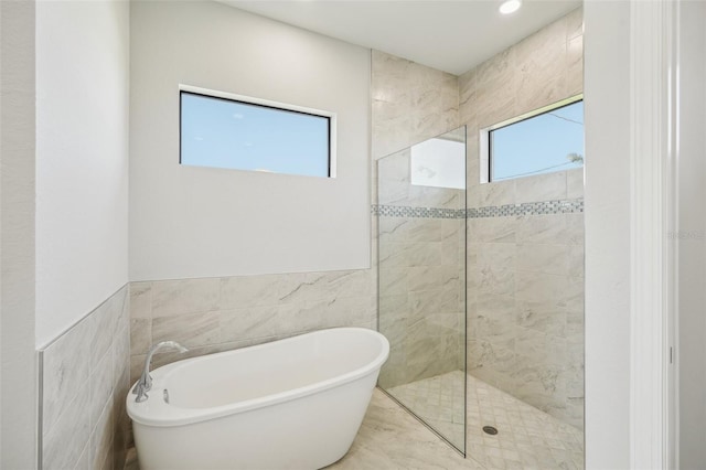 bathroom featuring a wealth of natural light, independent shower and bath, and tile walls