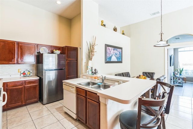 kitchen with white dishwasher, a breakfast bar area, sink, an island with sink, and stainless steel fridge