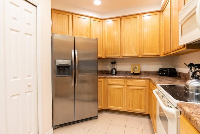 kitchen featuring white appliances, dark stone countertops, light brown cabinetry, and light tile patterned flooring