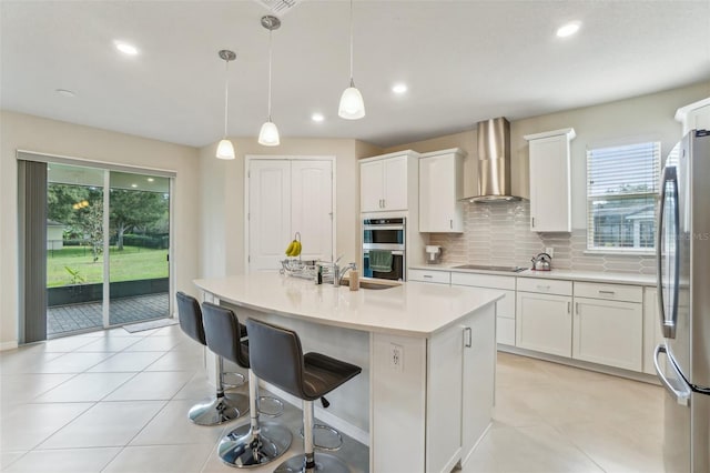 kitchen with a kitchen island with sink, wall chimney range hood, plenty of natural light, and pendant lighting