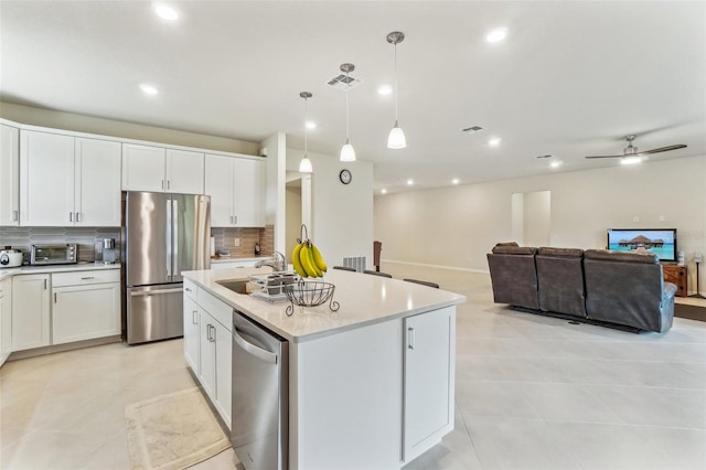 kitchen with tasteful backsplash, a center island with sink, appliances with stainless steel finishes, decorative light fixtures, and white cabinets