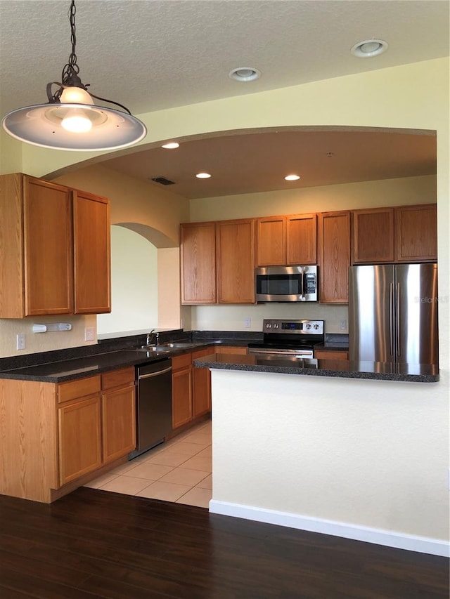 kitchen with appliances with stainless steel finishes, a textured ceiling, hanging light fixtures, sink, and light hardwood / wood-style flooring