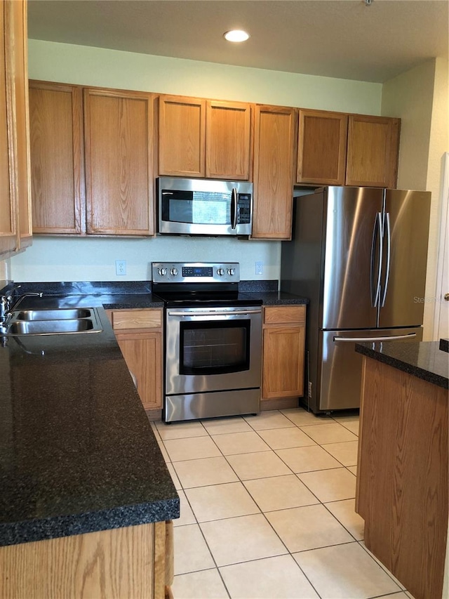 kitchen featuring stainless steel appliances, light tile patterned floors, sink, and dark stone counters