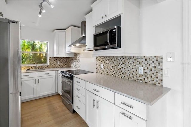 kitchen featuring white cabinets, wall chimney range hood, light hardwood / wood-style flooring, and appliances with stainless steel finishes