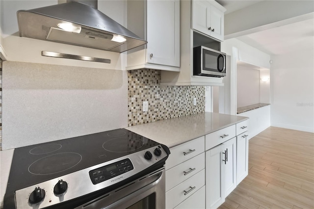 kitchen featuring backsplash, white cabinetry, appliances with stainless steel finishes, light hardwood / wood-style floors, and wall chimney exhaust hood