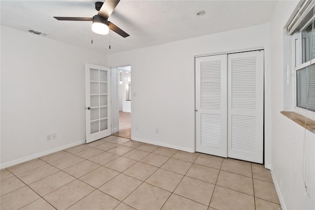 unfurnished bedroom with light tile patterned floors, ceiling fan, a closet, and french doors