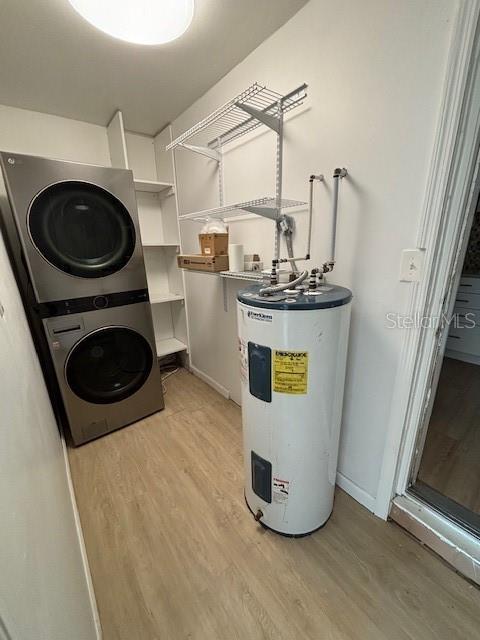 laundry area with stacked washer / drying machine, light hardwood / wood-style flooring, and water heater