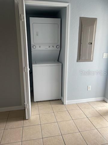 laundry room featuring electric panel, light tile patterned flooring, and stacked washer / drying machine