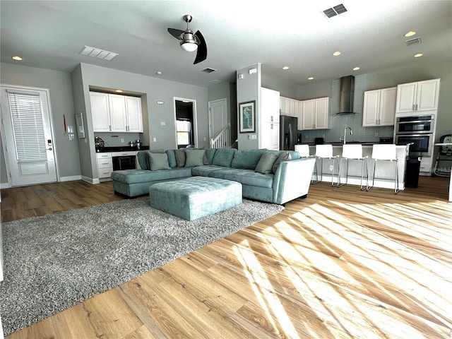 living room with wine cooler, ceiling fan, sink, and light hardwood / wood-style floors