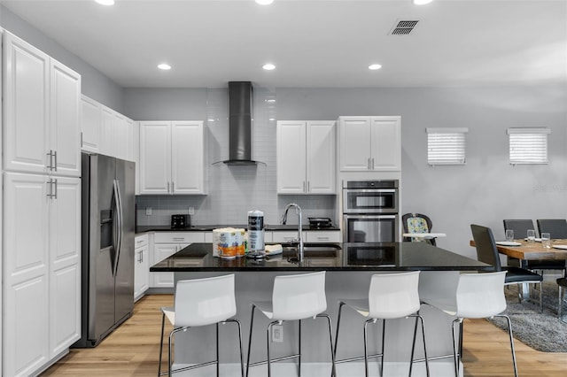 kitchen featuring white cabinetry, a center island with sink, wall chimney exhaust hood, and appliances with stainless steel finishes