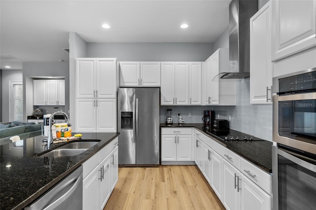 kitchen featuring sink, wall chimney exhaust hood, stainless steel appliances, dark stone countertops, and white cabinets