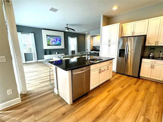 kitchen with light wood-type flooring, stainless steel appliances, a kitchen island with sink, and sink