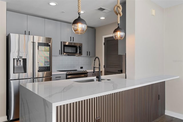 kitchen with pendant lighting, sink, light stone countertops, and stainless steel appliances