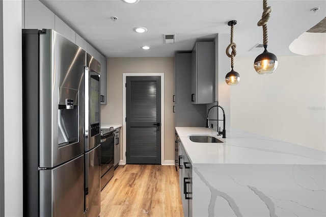 kitchen featuring stainless steel appliances, light hardwood / wood-style floors, sink, light stone counters, and hanging light fixtures