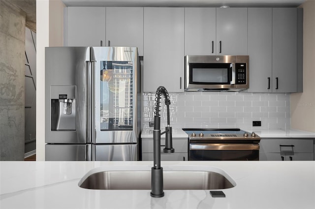 kitchen featuring appliances with stainless steel finishes, tasteful backsplash, gray cabinetry, and light stone countertops