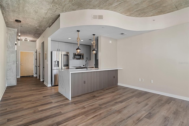 kitchen with stainless steel appliances, pendant lighting, kitchen peninsula, dark hardwood / wood-style floors, and white cabinetry