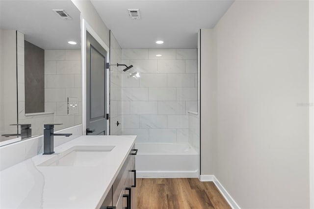 bathroom with wood-type flooring, vanity, and tiled shower / bath