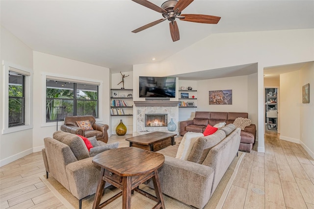 living room with vaulted ceiling, light hardwood / wood-style flooring, built in shelves, ceiling fan, and a premium fireplace