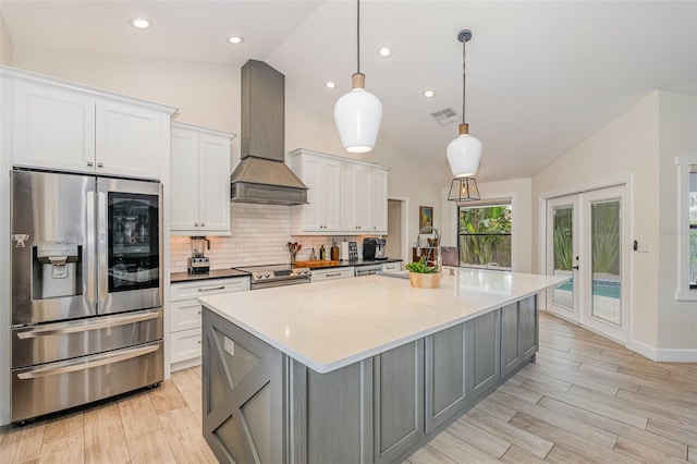 kitchen featuring wall chimney exhaust hood, stainless steel appliances, vaulted ceiling, pendant lighting, and white cabinets