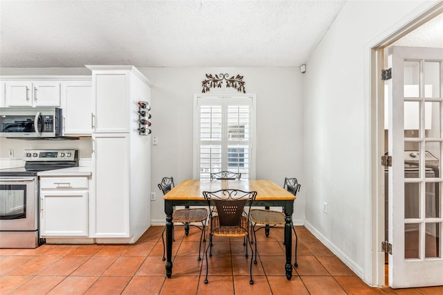 kitchen featuring a textured ceiling, stainless steel appliances, white cabinetry, and light tile patterned flooring