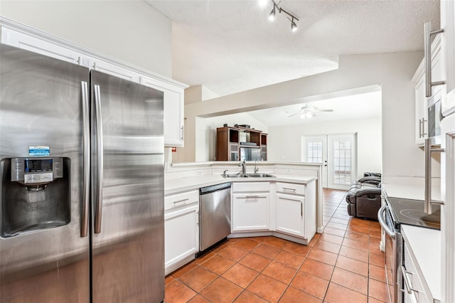 kitchen with kitchen peninsula, stainless steel appliances, vaulted ceiling, sink, and white cabinets