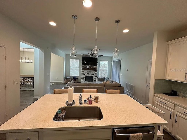 kitchen featuring light stone counters, dark wood-type flooring, pendant lighting, white cabinetry, and an island with sink