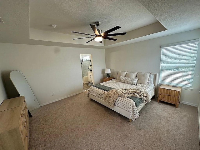 carpeted bedroom featuring a textured ceiling, ceiling fan, ensuite bathroom, and a tray ceiling