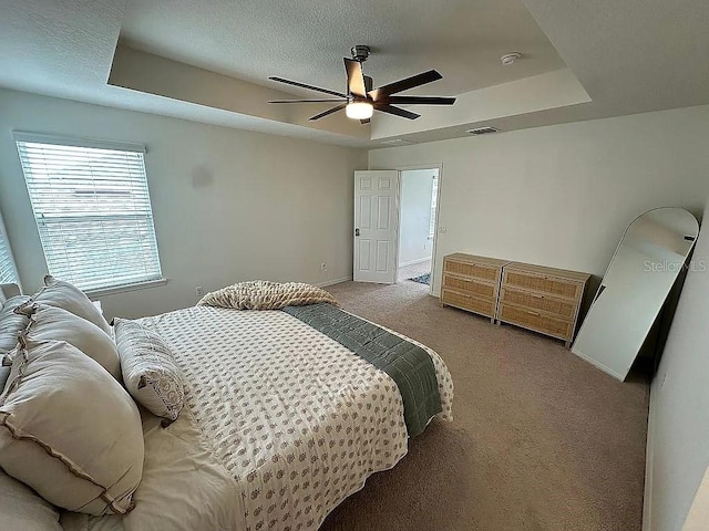 carpeted bedroom featuring ensuite bathroom, a raised ceiling, and ceiling fan