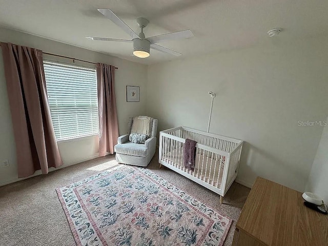 carpeted bedroom with ceiling fan and a crib