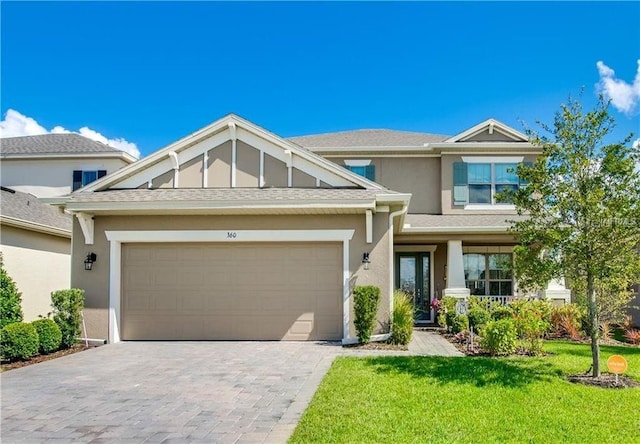 craftsman house featuring a front yard, roof with shingles, stucco siding, a garage, and decorative driveway