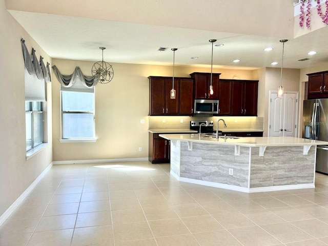 kitchen with a kitchen island with sink, a sink, stainless steel appliances, light countertops, and decorative backsplash