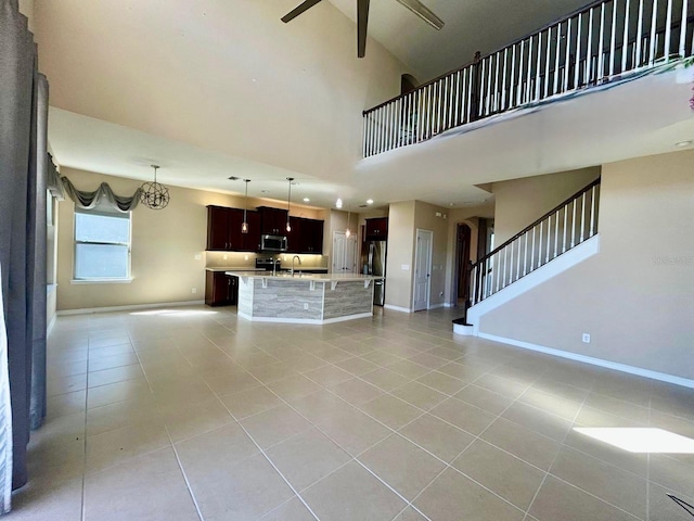 unfurnished living room with stairs, light tile patterned flooring, baseboards, and a towering ceiling