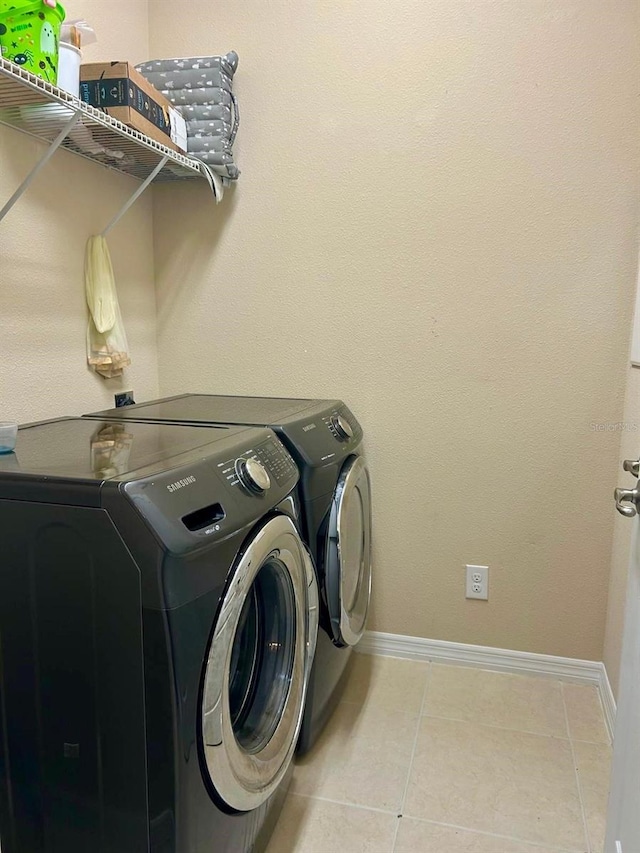 washroom with light tile patterned flooring, laundry area, washer and dryer, and baseboards