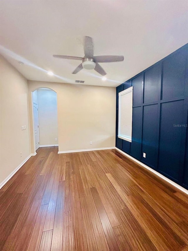 unfurnished room featuring a ceiling fan, wood finished floors, visible vents, baseboards, and arched walkways