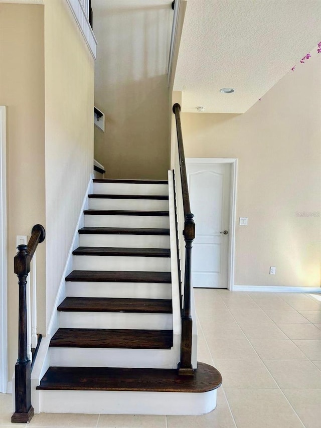 stairway with tile patterned flooring, baseboards, and a textured ceiling