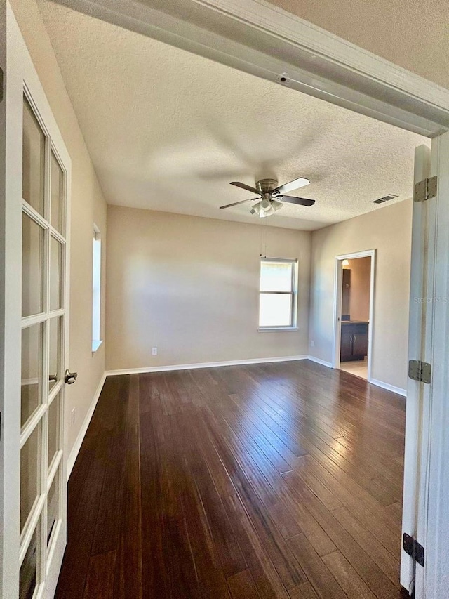 empty room featuring a ceiling fan, baseboards, visible vents, hardwood / wood-style flooring, and a textured ceiling