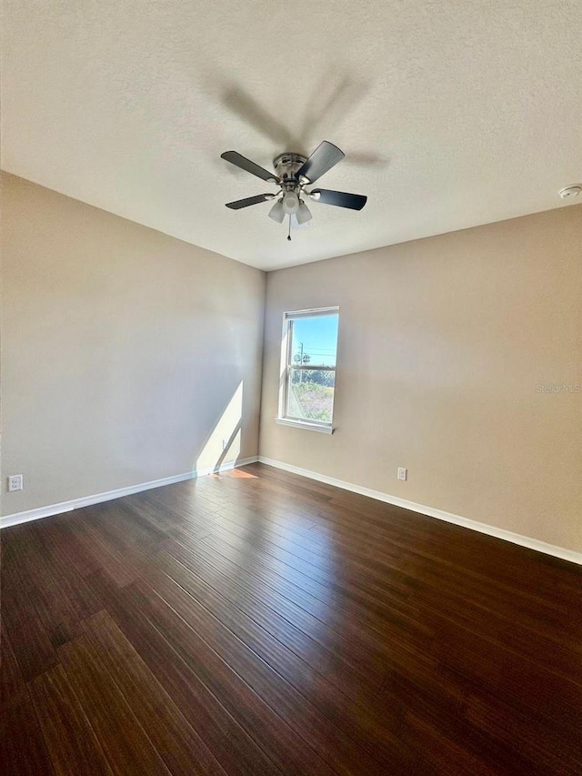 empty room with a textured ceiling, a ceiling fan, baseboards, and dark wood-style flooring