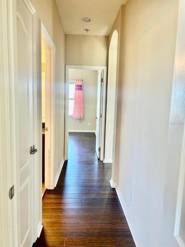 hall with arched walkways, baseboards, and dark wood-style flooring