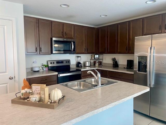 kitchen with a kitchen island with sink, sink, dark brown cabinets, and appliances with stainless steel finishes