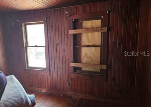 bedroom featuring multiple windows, wood-type flooring, and wooden walls