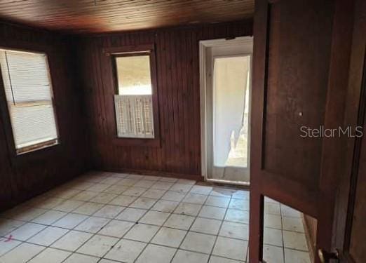 unfurnished room with wood walls, light tile patterned floors, and wooden ceiling