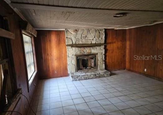 unfurnished living room featuring wooden ceiling, a stone fireplace, light tile patterned floors, and wood walls