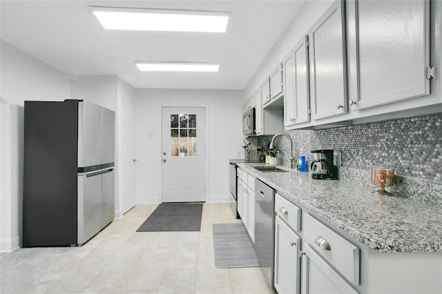 kitchen featuring stainless steel appliances, sink, light stone countertops, light tile patterned floors, and backsplash