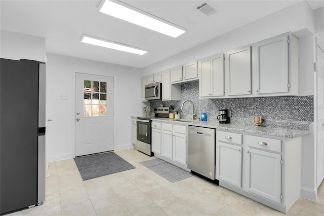 kitchen with light tile patterned flooring, backsplash, appliances with stainless steel finishes, sink, and white cabinets