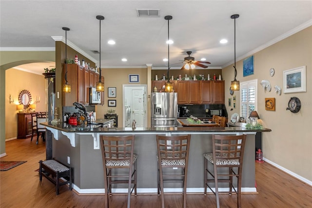 kitchen featuring kitchen peninsula, appliances with stainless steel finishes, a kitchen breakfast bar, hardwood / wood-style flooring, and hanging light fixtures