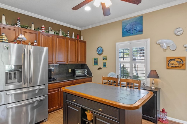 kitchen with stainless steel refrigerator with ice dispenser, tasteful backsplash, ornamental molding, a kitchen island, and tile counters