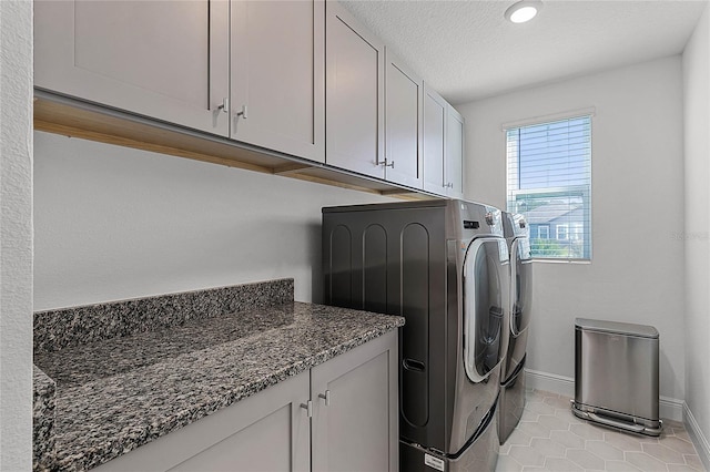 clothes washing area with cabinet space, baseboards, a textured ceiling, washer and dryer, and light tile patterned flooring