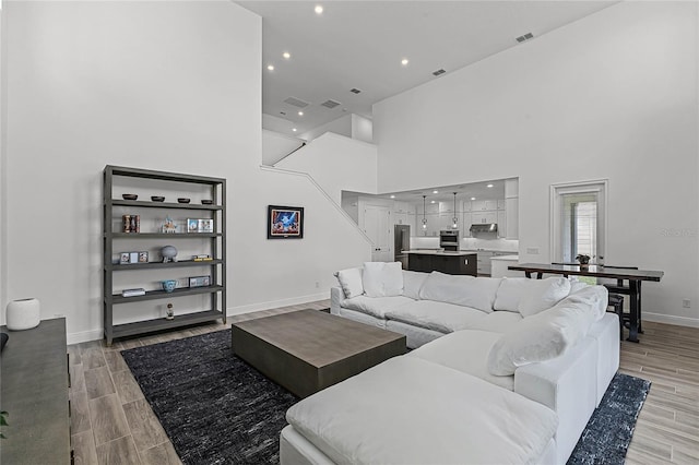 living area with visible vents, recessed lighting, a high ceiling, baseboards, and wood tiled floor